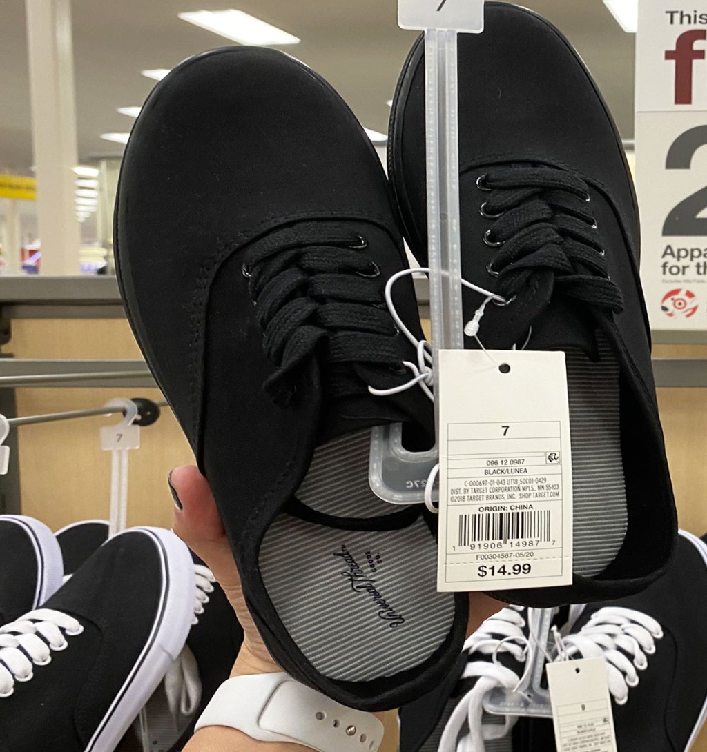 person holding up a black pair of universal threads sneakers at target