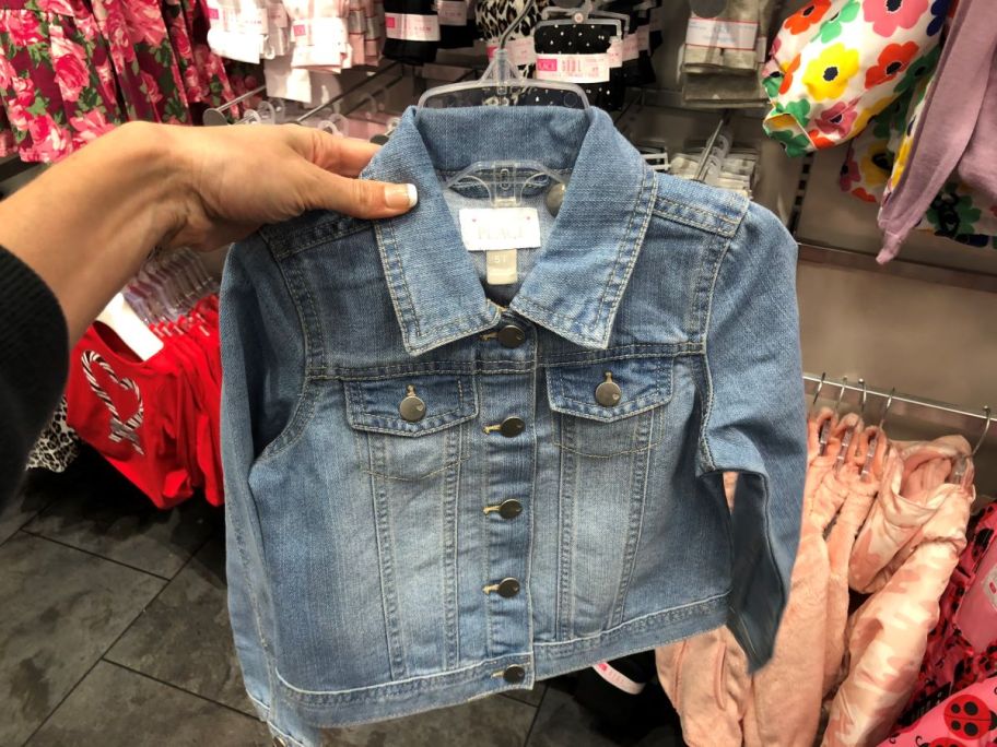 hand holding a denim jacket on a hanger