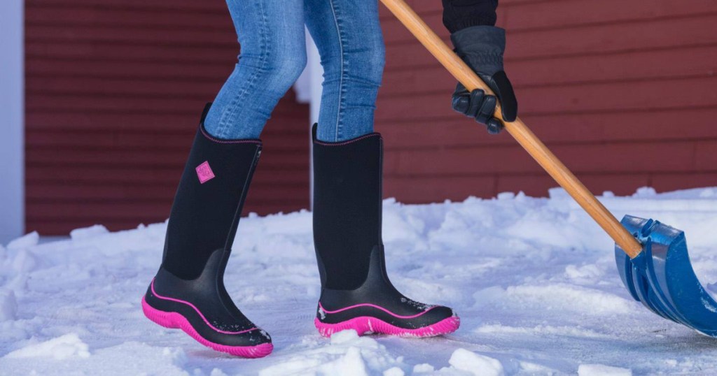 woman shoveling snow and wearing jeans and black and hot pink tall boots