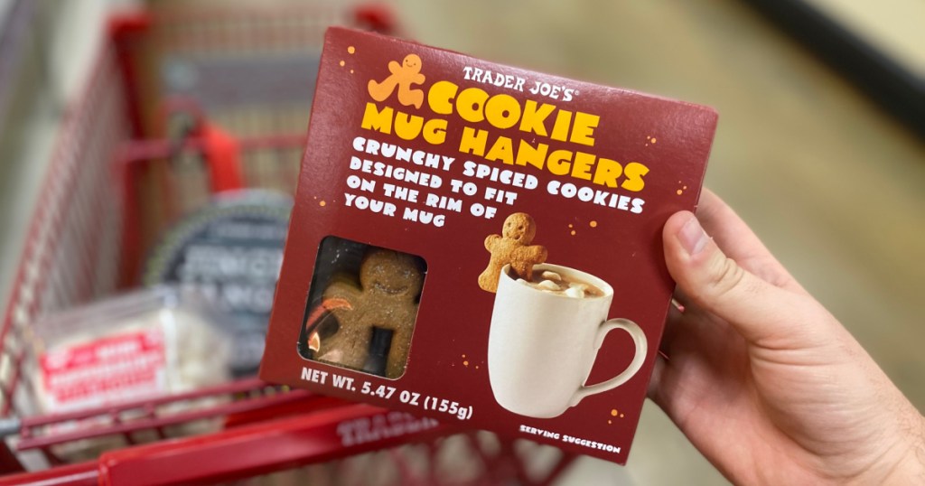 hand holding box of cookie mug hangers in front of cart full of items in store