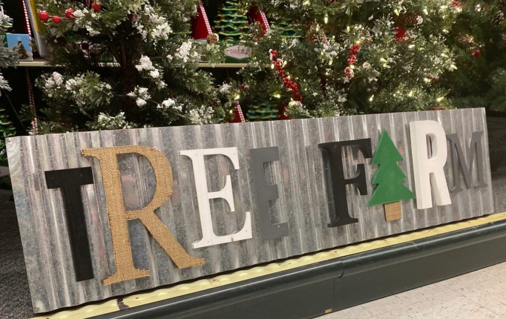 large tree farm wall sign in front of Christmas trees in store