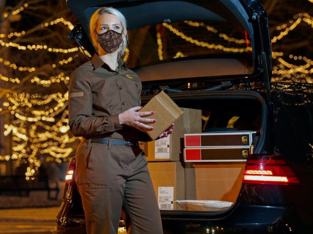 woman ups driver standing behind a car holding a package