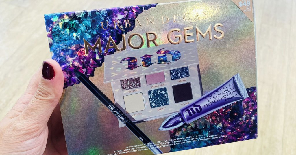 woman with dark red nails holding up the urban decay major gems makeup set