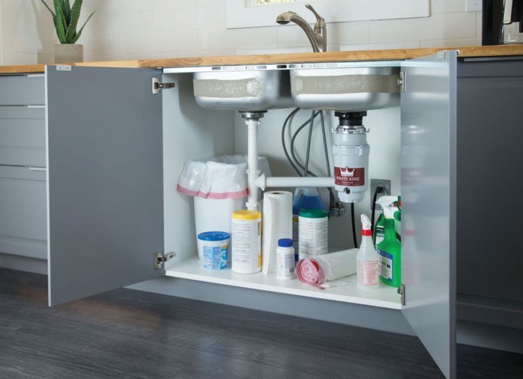 under-sink cabinet doors opened to show garbage disposal, trash can, and cleaning products under sink