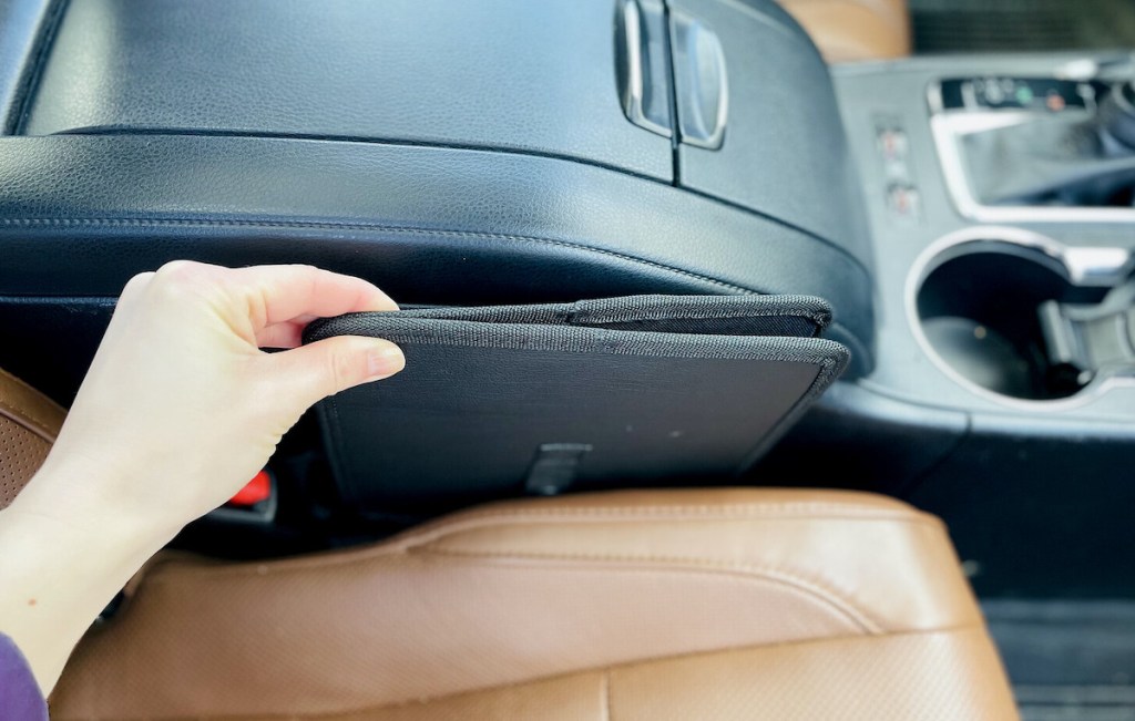 hand holding collapsible trash can between car seat and console