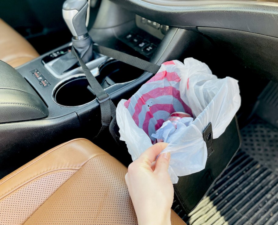 hand holding edge of mini trash can, one of our car organizer ideas, hanging over car floor