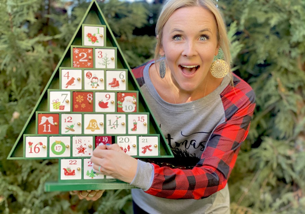 woman holding advent calendar in front of green trees