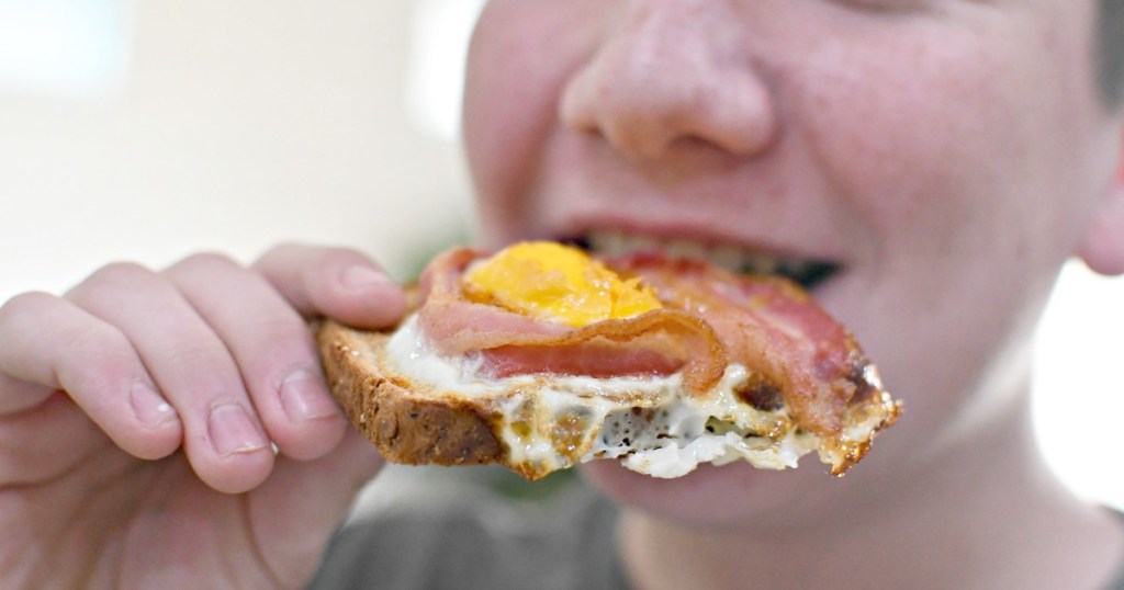 boy eating toast with an egg and bacon on top