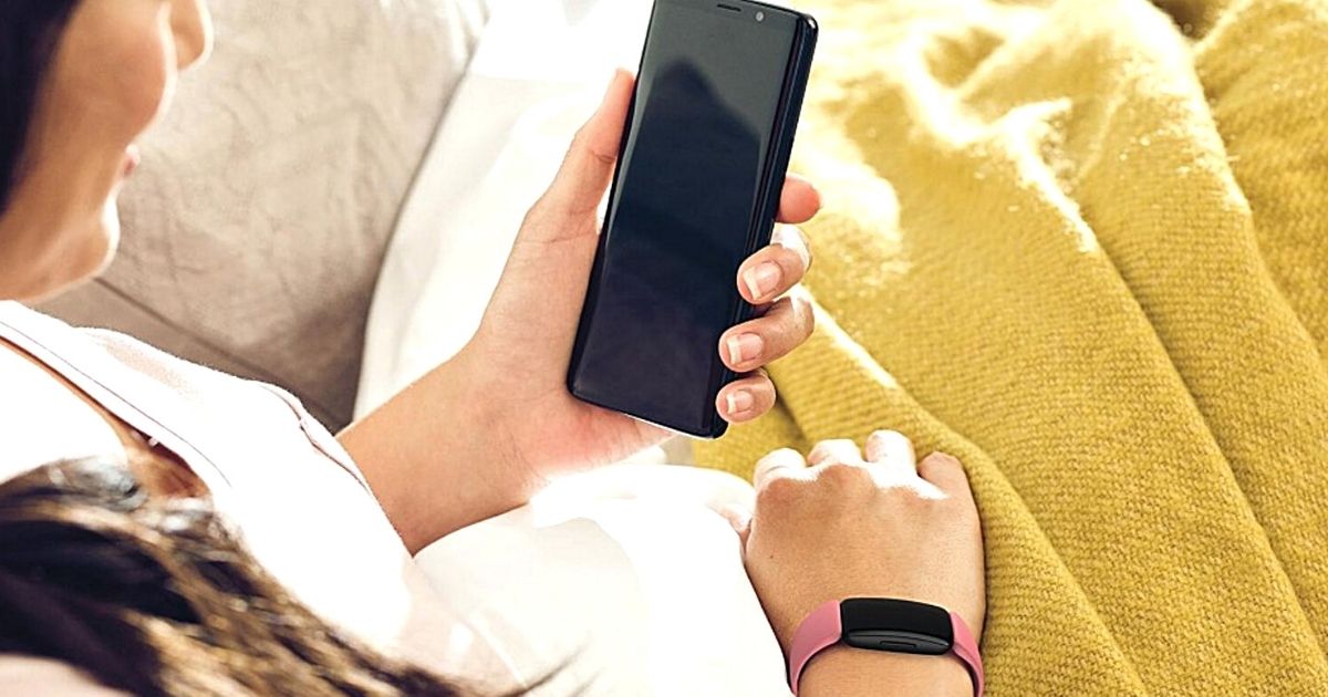 woman looking at phone and wearing pink fitbit