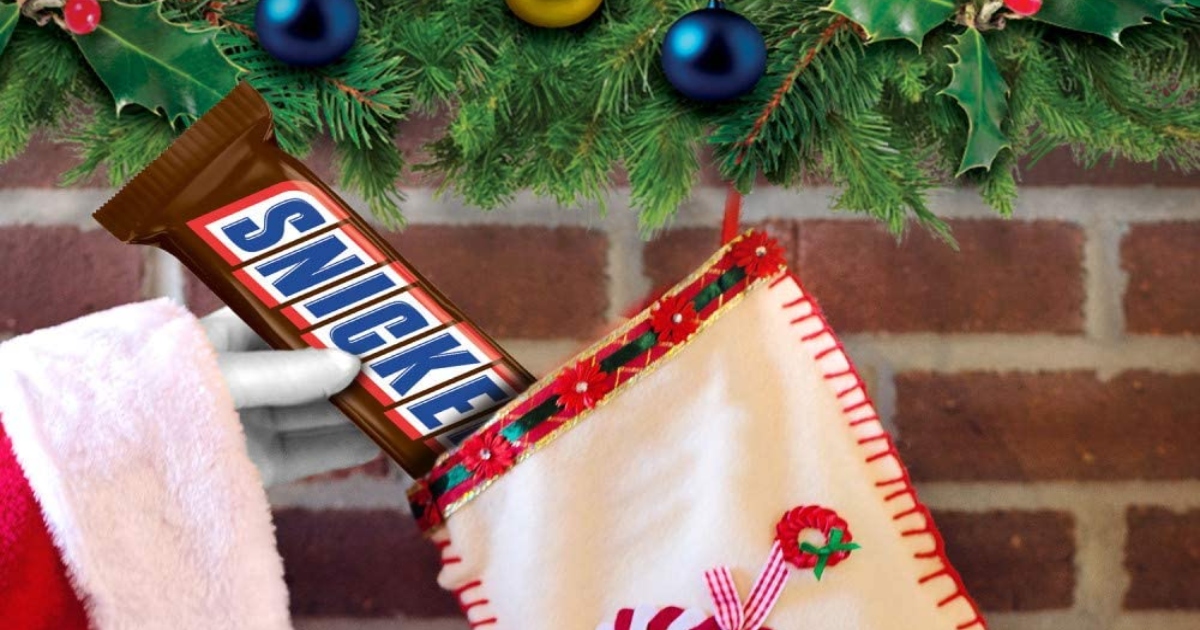 santa hand putting a giant snickers bar in a stocking