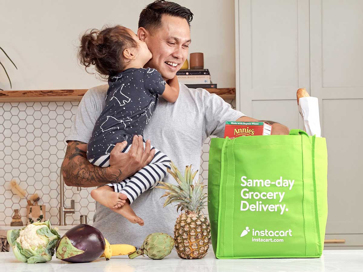 man holding a small child lookinginto a instacart shopping bag