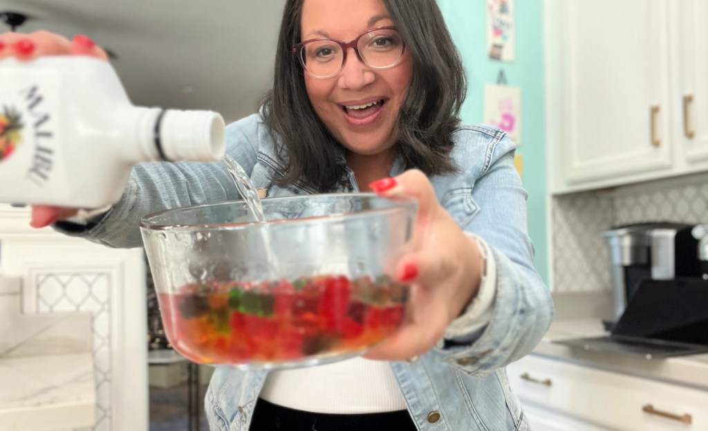 pouring rum over gummy bears in a glass bowl