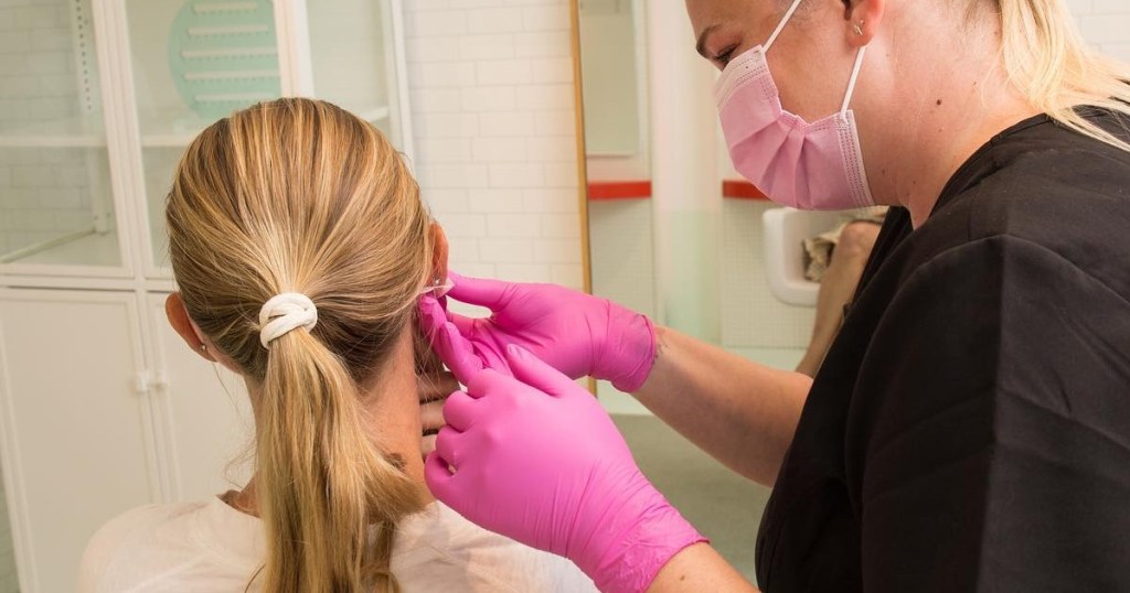 girl getting ears pierced by masked nurse