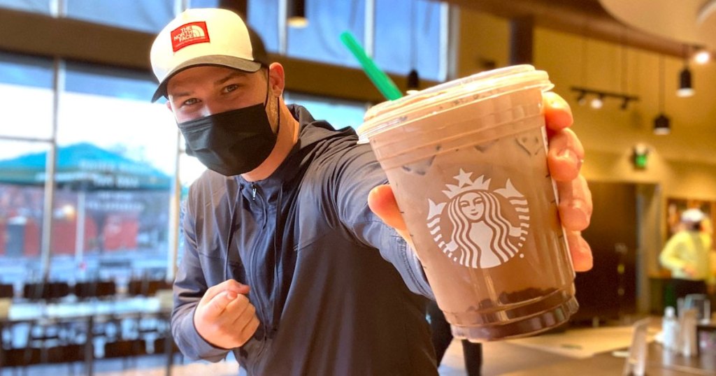 man holding starbucks cookies and cream cold brew drink with mask on his face
