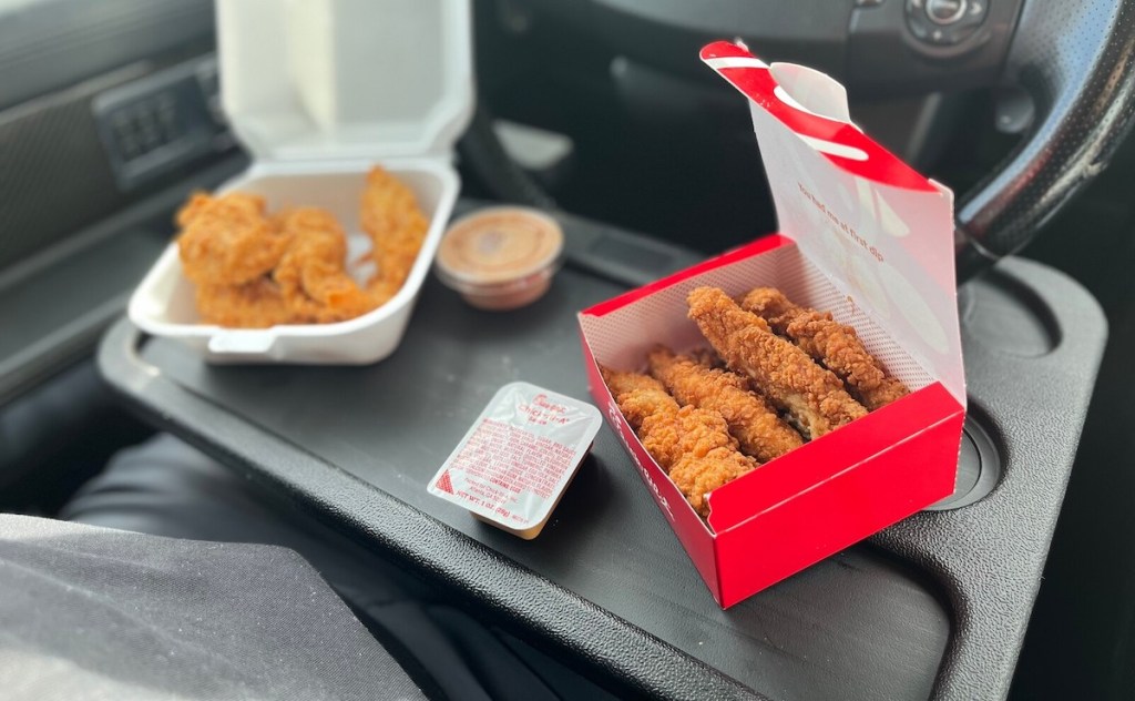 take out food with chicken tenders and chick fil a sauce on steering wheel tray