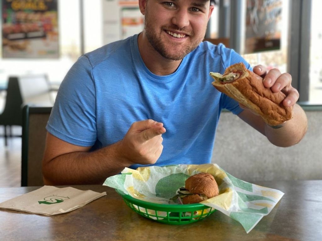 man sitting at a table inside subway eating a sub