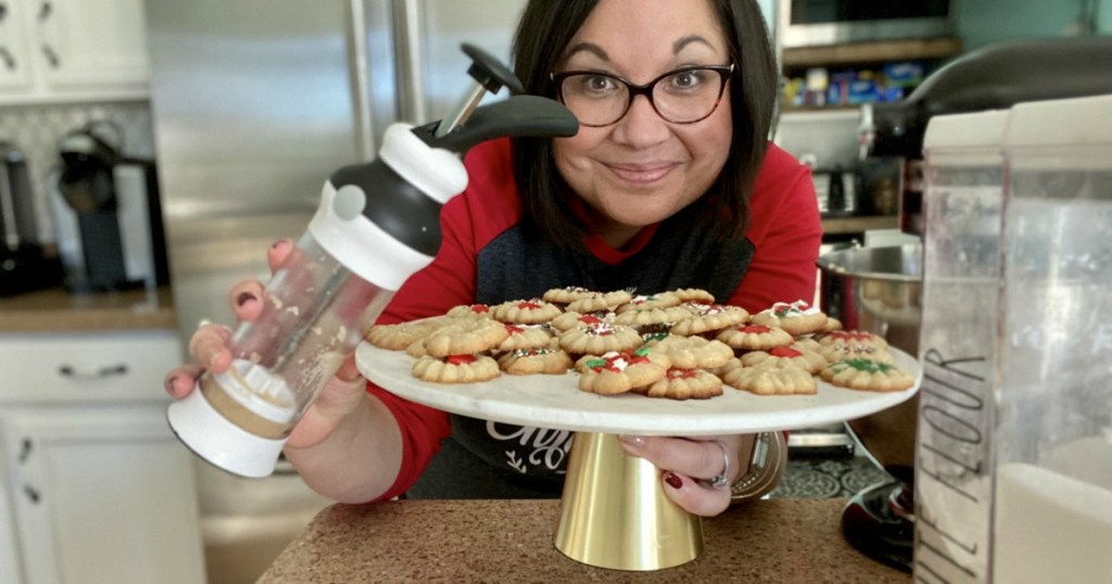 woman holding a cookie press and plate of cookies