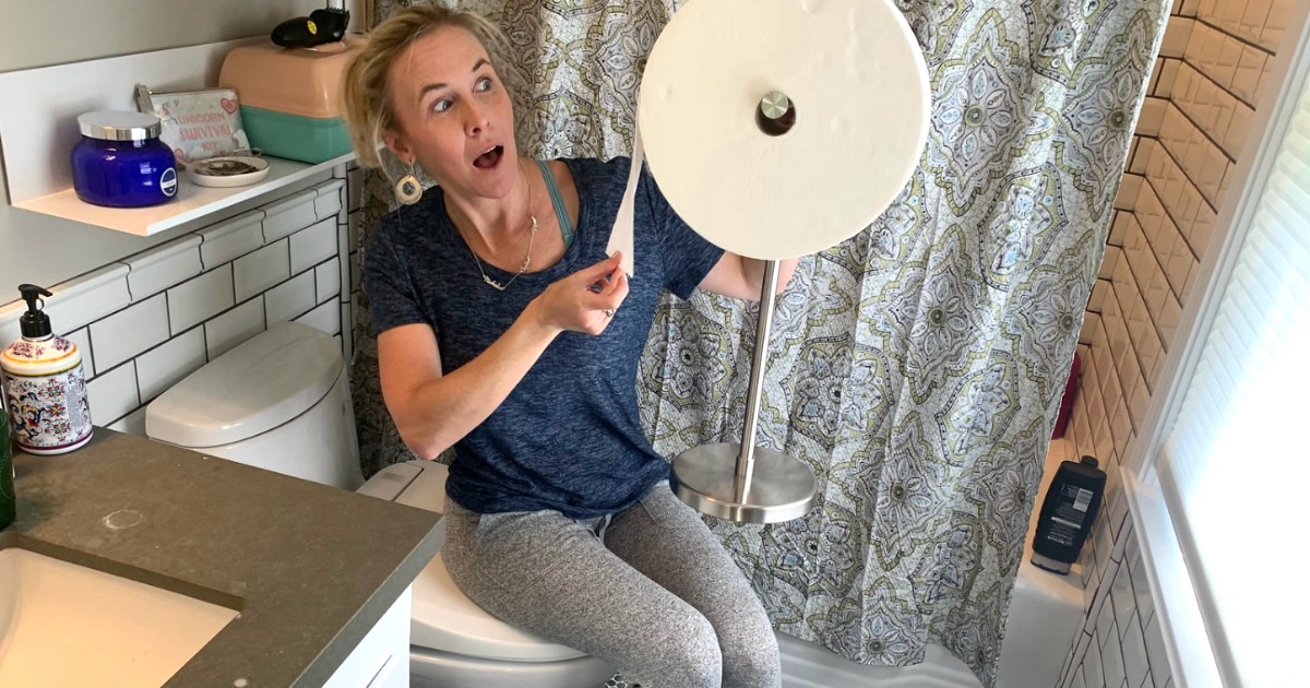 woman holding large roll of toilet paper in bathroom 