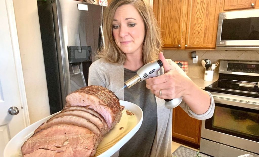 A woman searing a ham with a blow torch