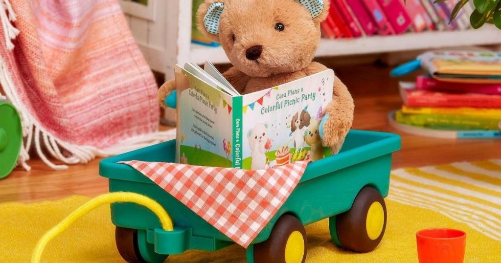 plush bear holding a book and sitting in a wagon