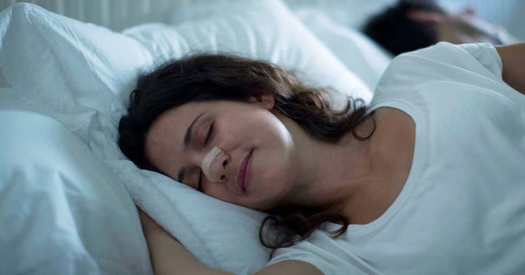 woman sleeping in bed with breathe right nasal strip on her nose