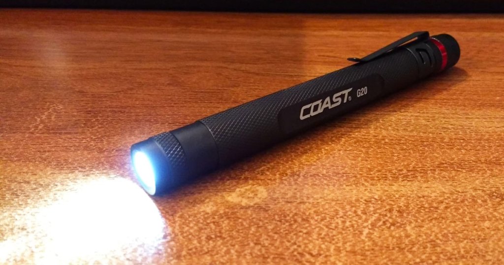black pen-sized flashlight laying on a wood table and shining it's light