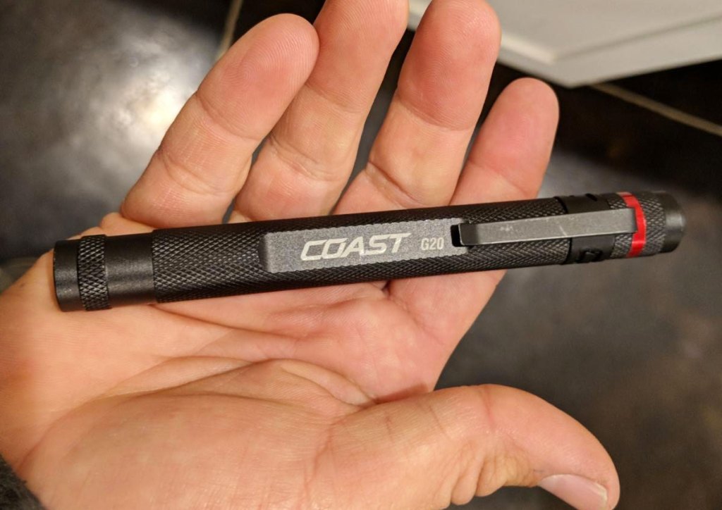 person holding a black pen-size flashlight in the palm of their hand