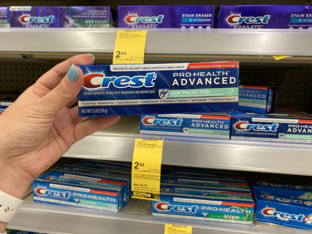 Crest toothpastes on Walgreens shelf with woman holding up a package