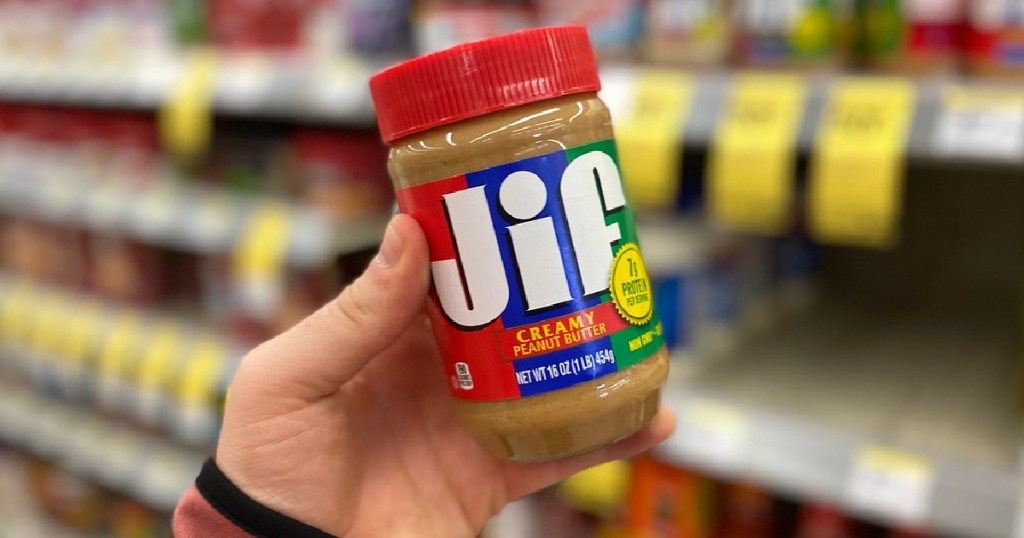 mans hand holding jar of peanut butter in store