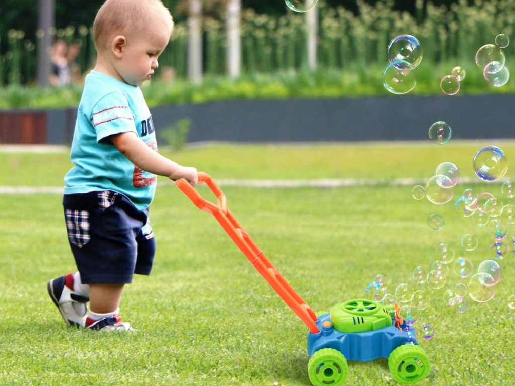 baby boy pushing a bubble mower outside in the grass