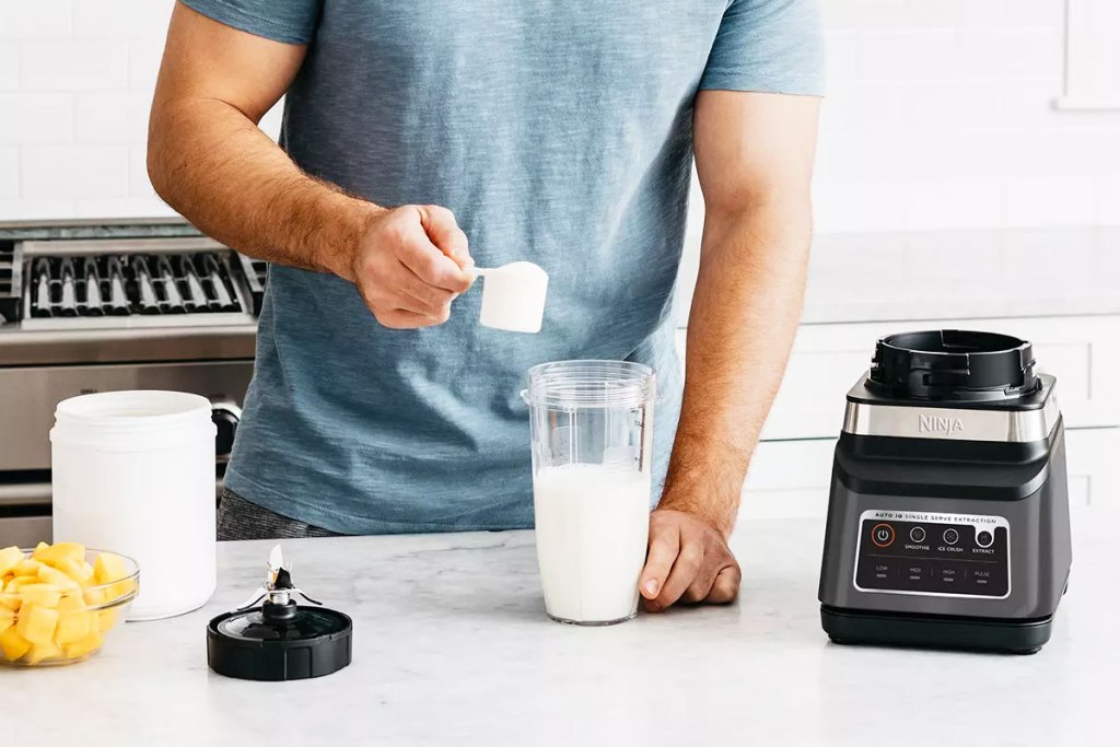 man adding protein powder to an individual blender cup next to the base for a ninja blender
