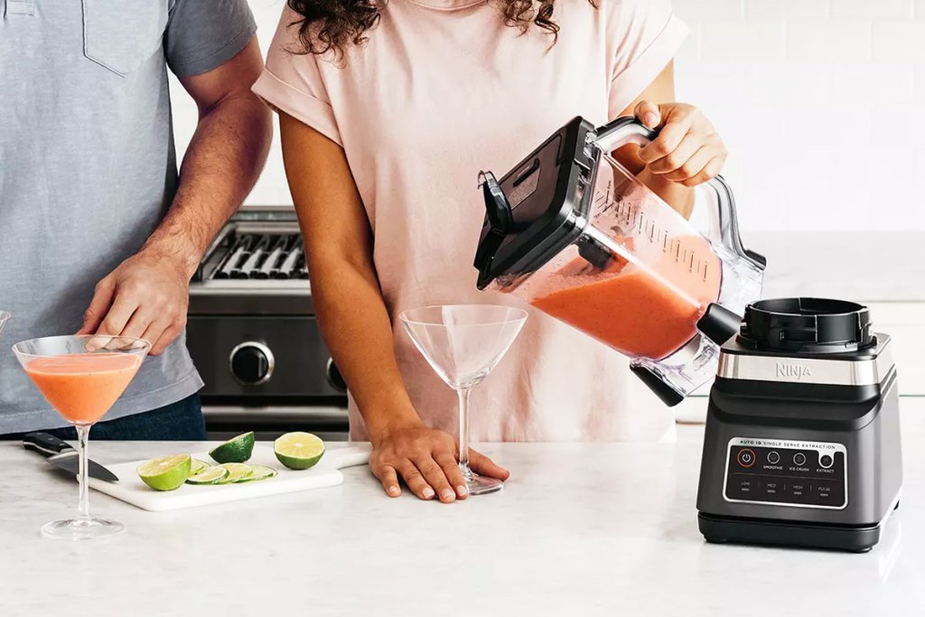 woman pouring strawberry daiquiri into glass from a ninja blender