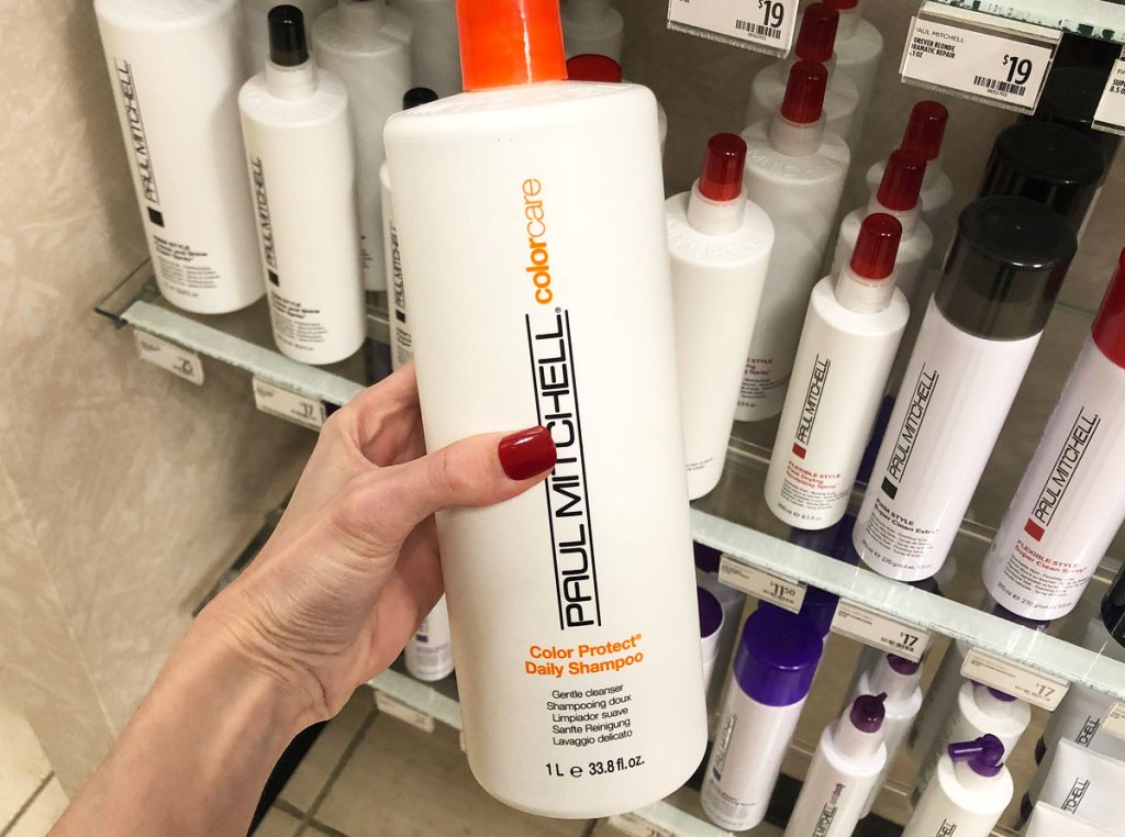 person holding up white and orange bottle of paul mitchell shampoo