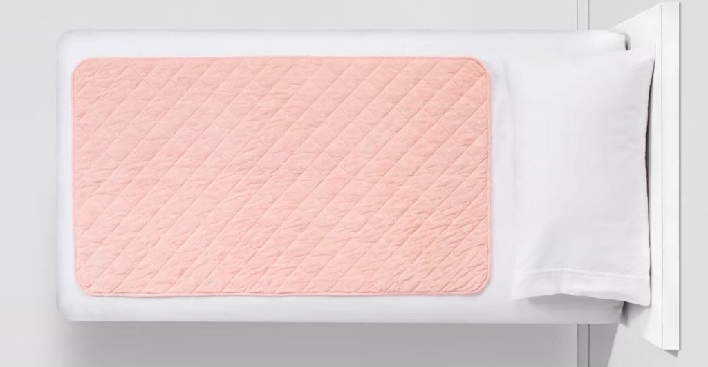 pink colored Pillowfort Waterproof Sleep Anywhere Pad on white bed
