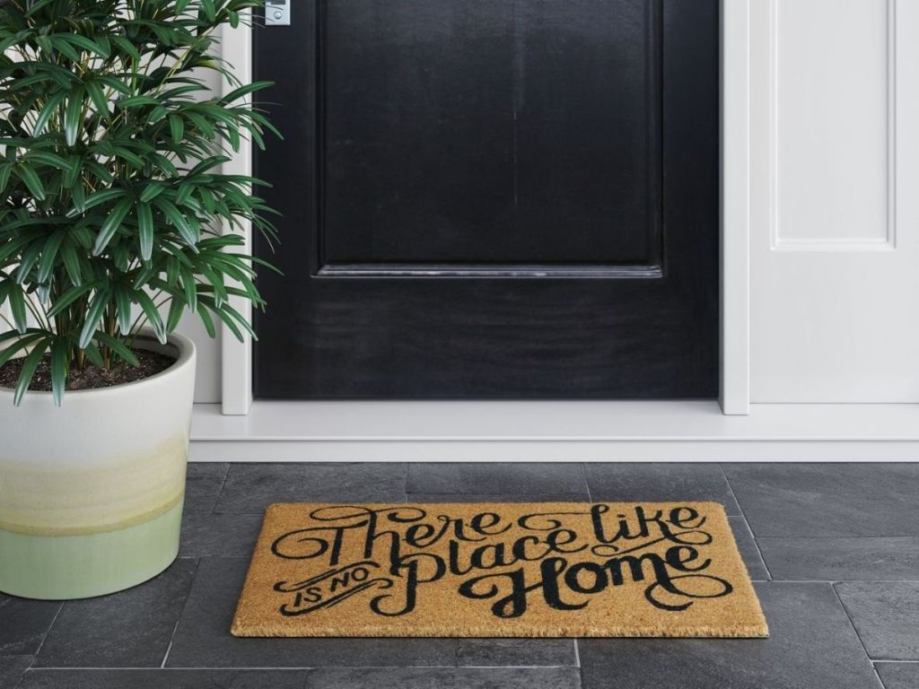 There's No Place Like Home Doormat in front of front door on porch next to a potted plant