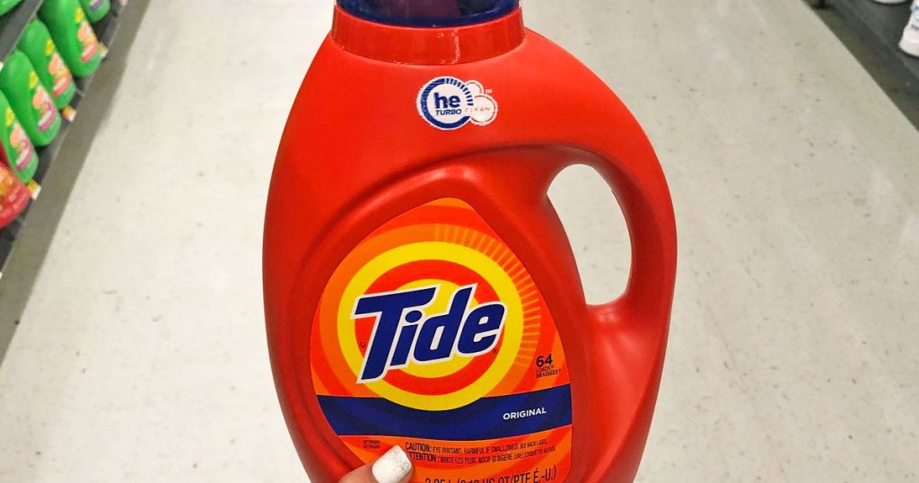 person with white finger nails holding up a bright orange bottle of tide liquid laundry detergent