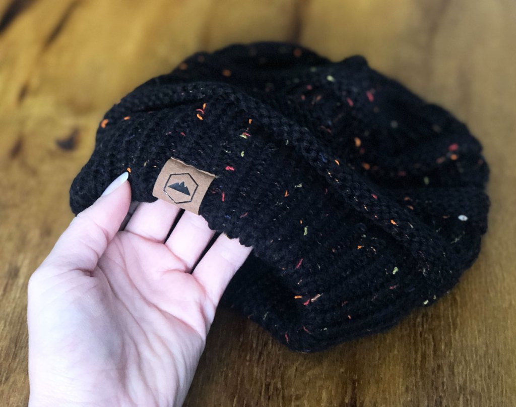 woman holding up brim of black cable knit beanie