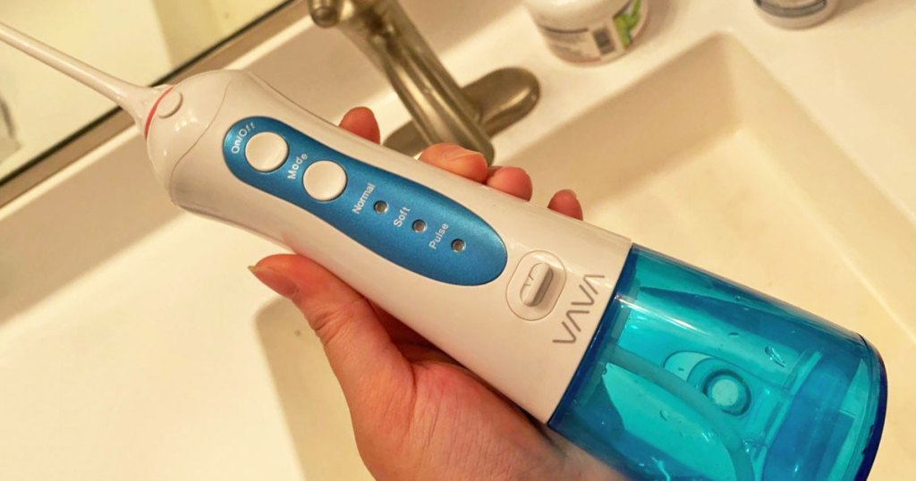 person holding up a white and blue cordless water flosser with bathroom sink in background