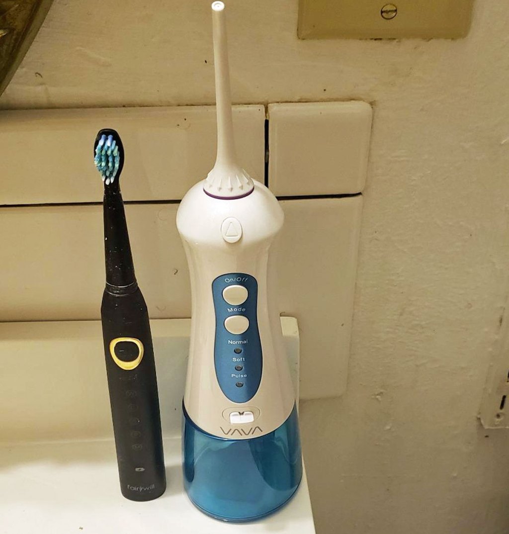 white and blue water flosser on bathroom counter next to black electric toothbrush