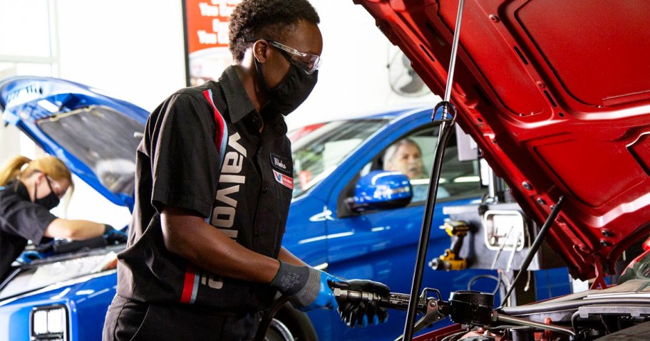 man wearing face mask adding oil into engine of a red car
