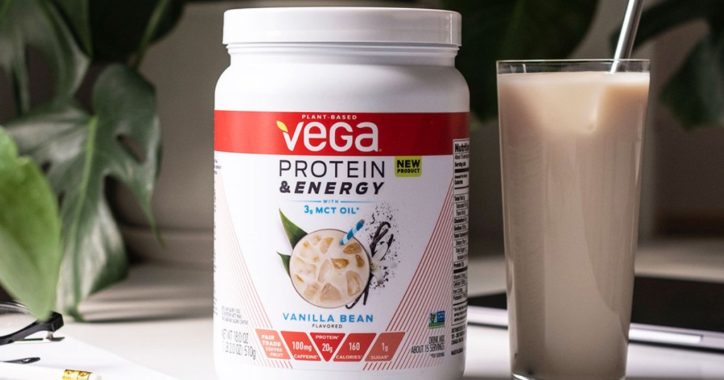 white and orange container of vega protein powder next to glass of protein shake with a straw in it
