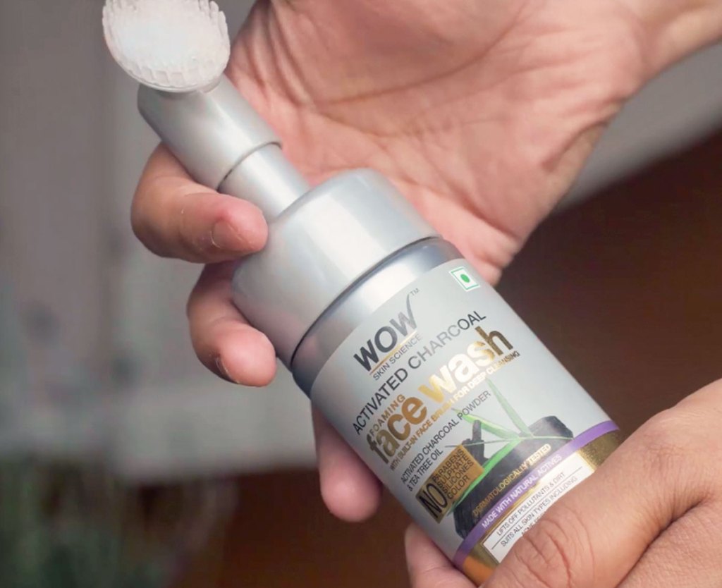person holding grey bottle of wow skincare science face wash with brush tip attached to top