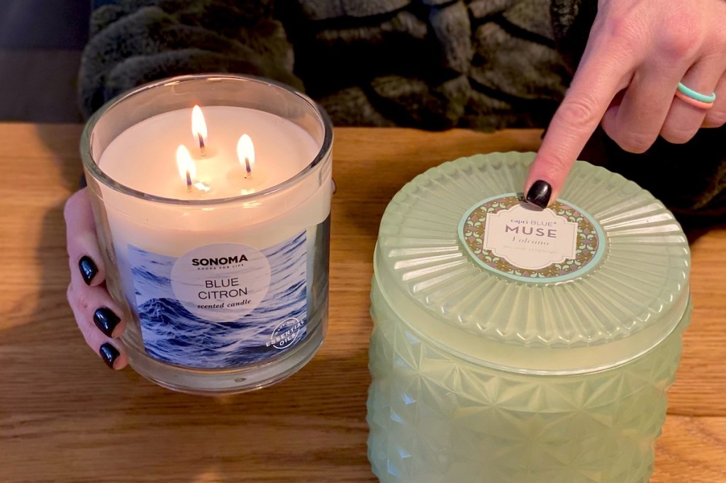 woman holding a lit 3 wick candle pointing to capri blue candle