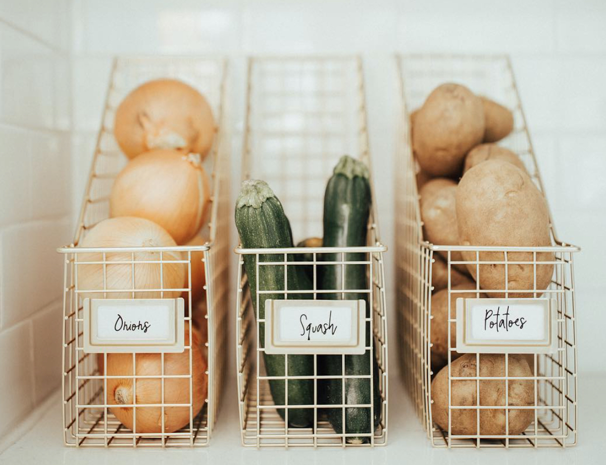 row of onions squash and potatoes on shelf in labeled wire magazine holders, one of our favorite pantry organizers