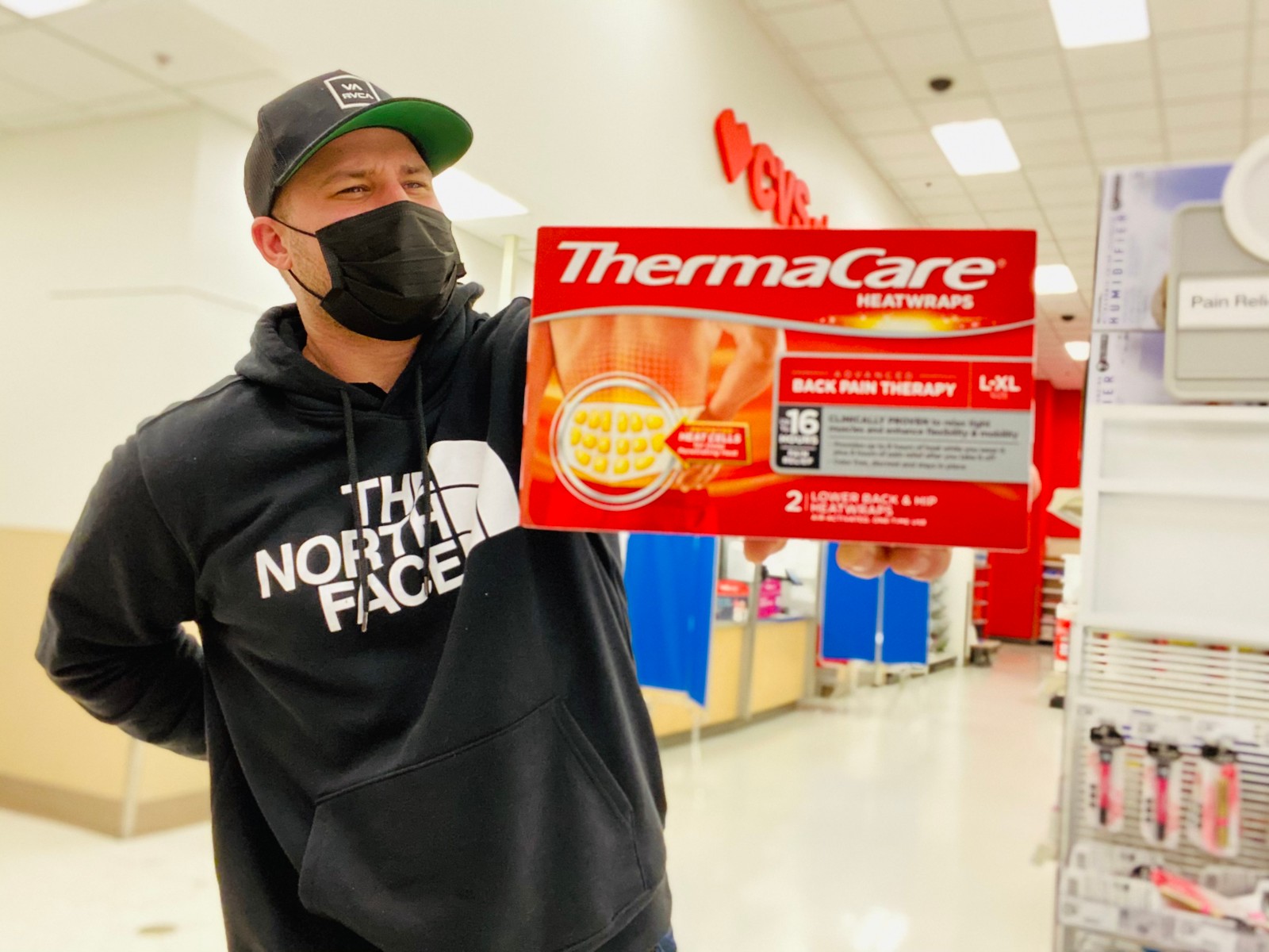 man holding Thermacare box while holding his back and grimacing in a cvs store