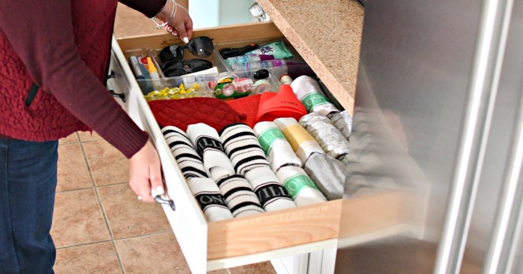 hand pulling out sunglasses from organized kitchen drawer with towels