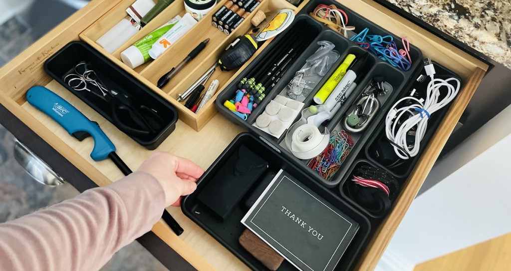 hand holding edge of plastic container inside junk drawer