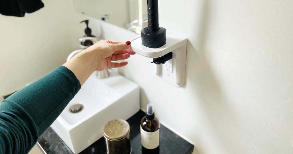 hand holding edge of white outlet shelf with electric toothbrush on top - bathroom storage ideas