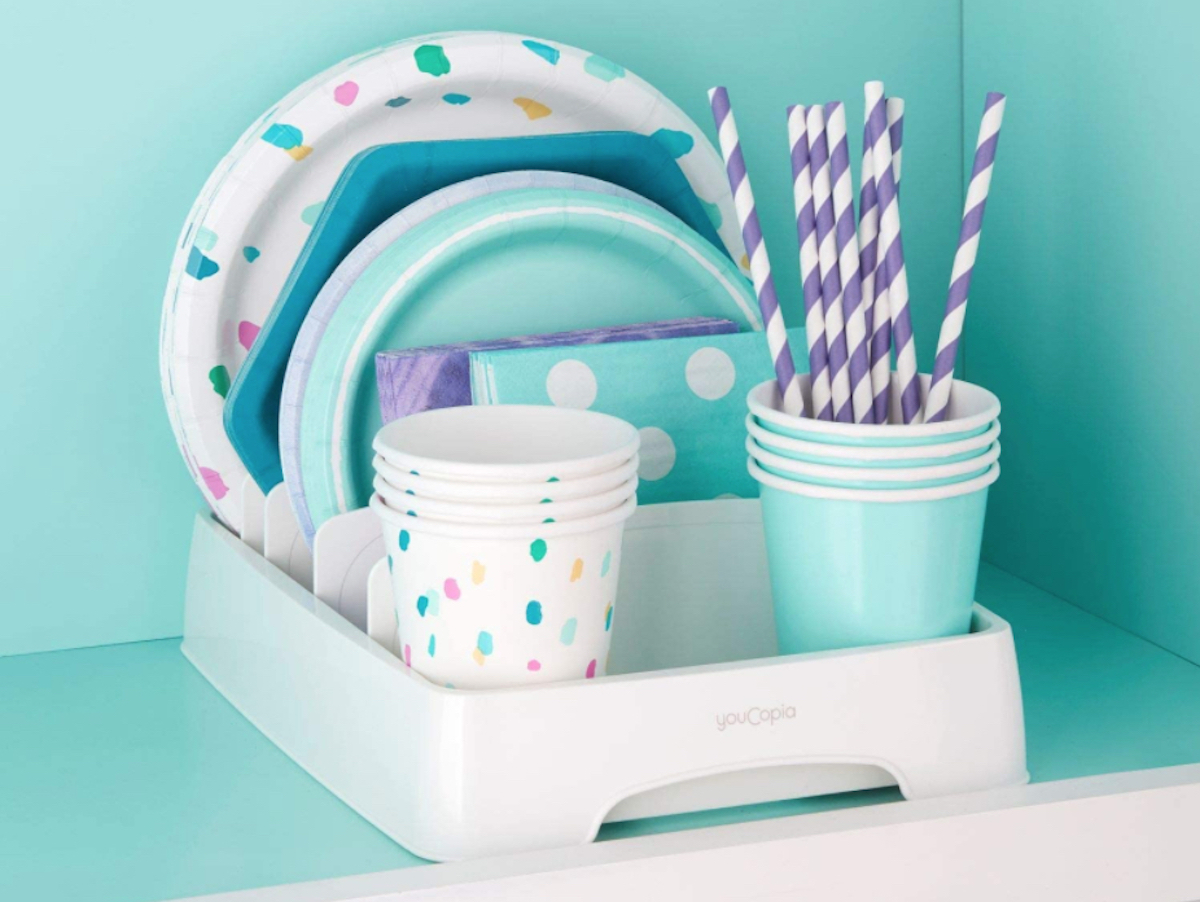 colorful party supplies in organizer on shelf with bright blue wall