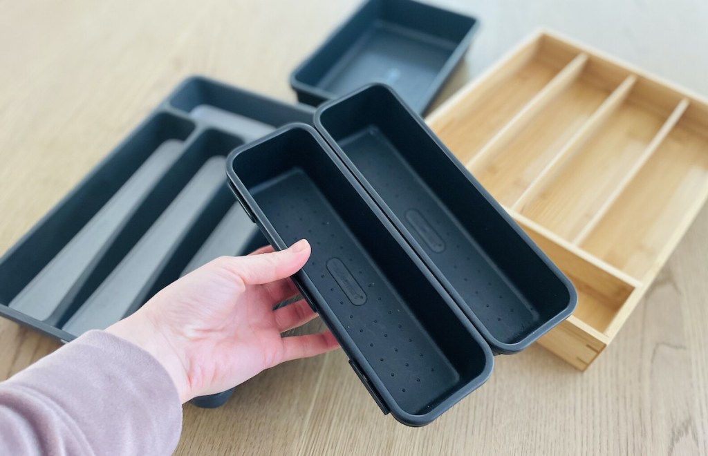 hand holding black plastic organizers over table full of drawer organizers